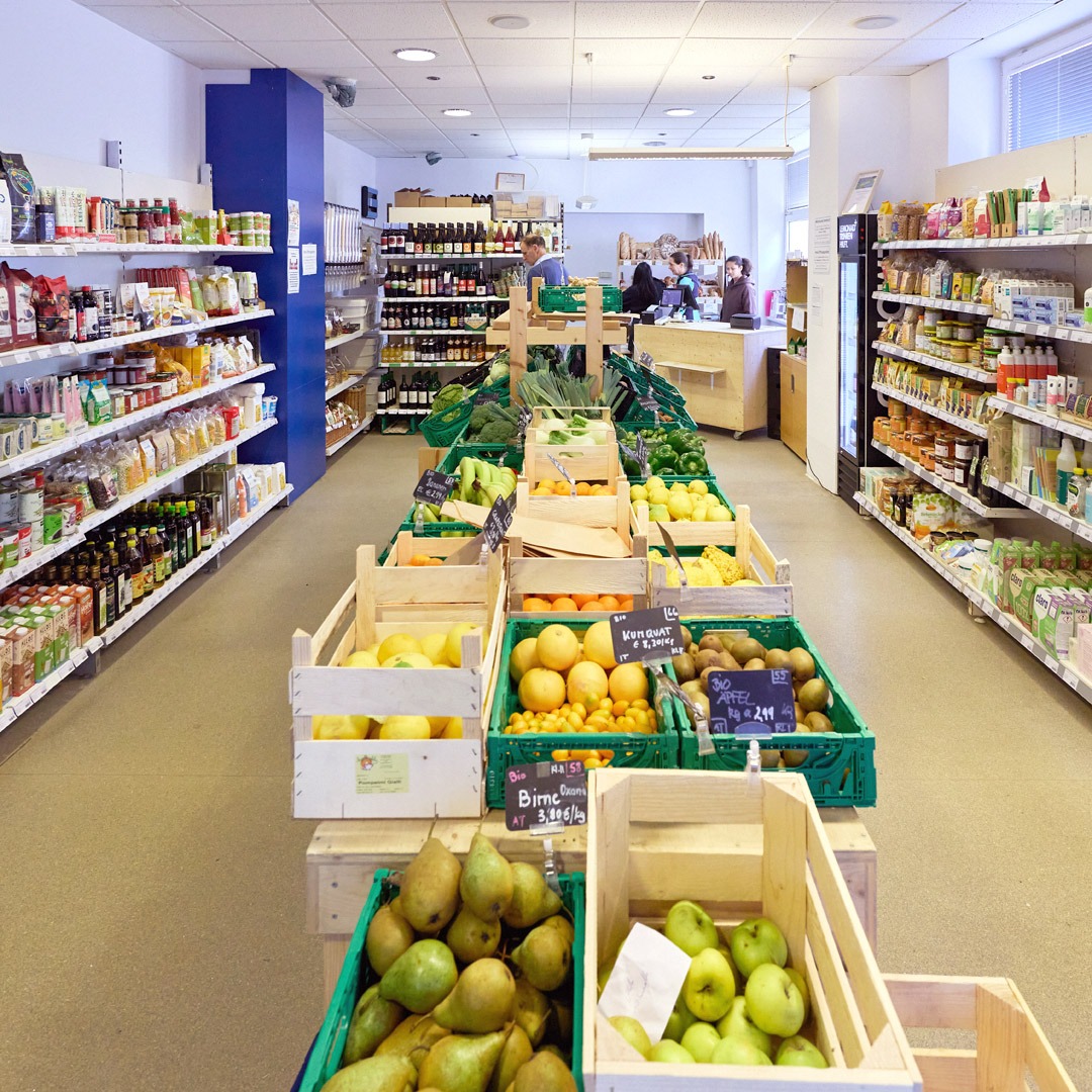 Ein Blick in den MILA-Minimarkt mit über 800 Produkten. In der Mitte viele Körbe mit frischem Obst und Gemüse