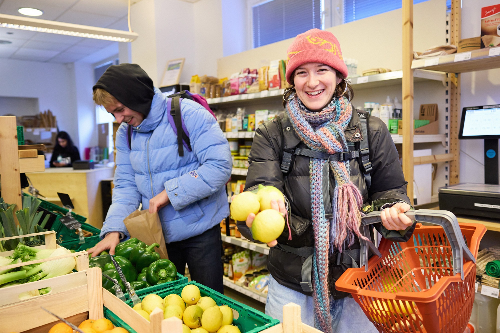Ein junge Frau mit Einkaufskorb zeigt ihre Zitronen im MILA-Minimarkt