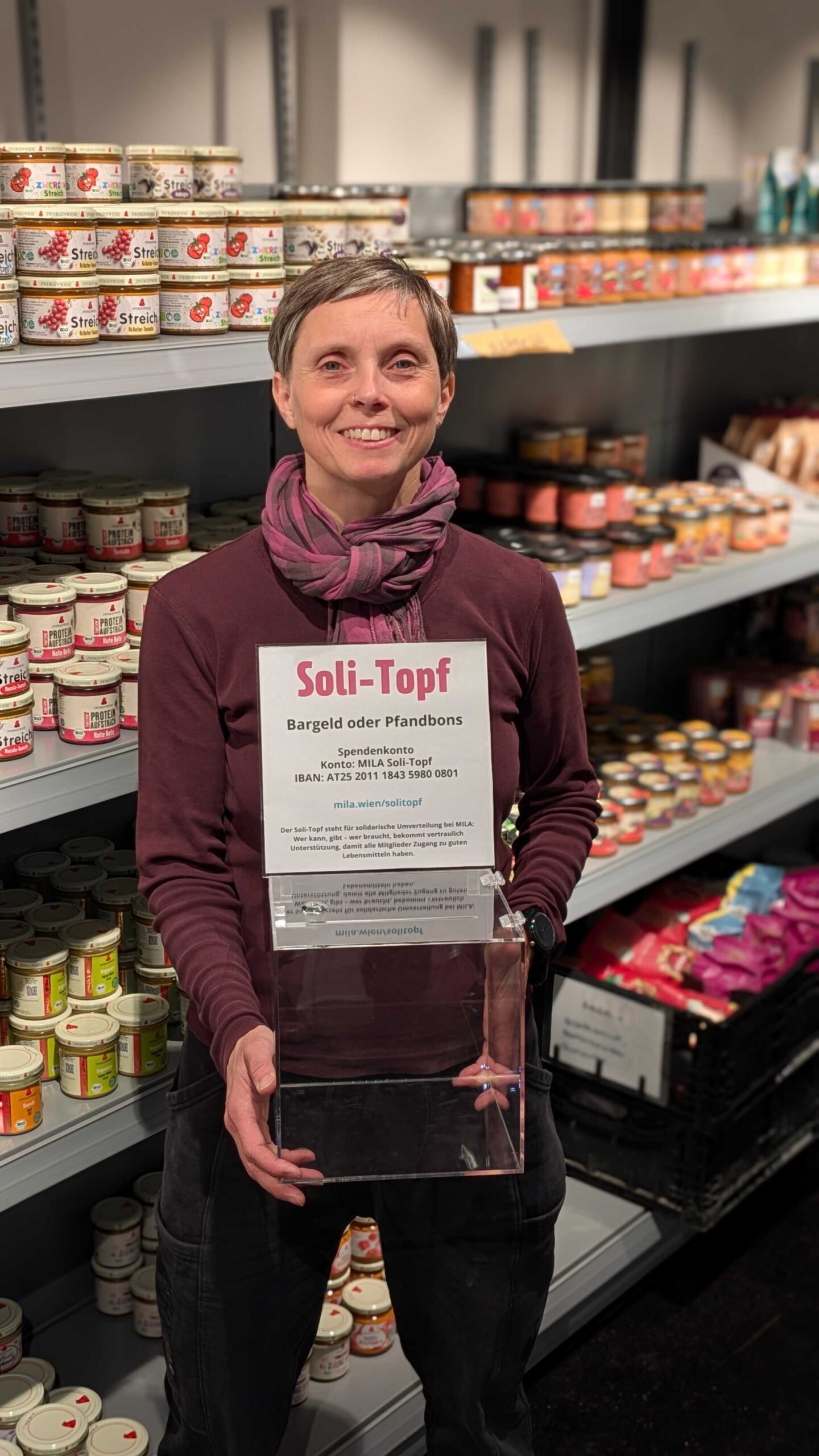 MILA Mitglied hält Glasbox vor gefülltem regal